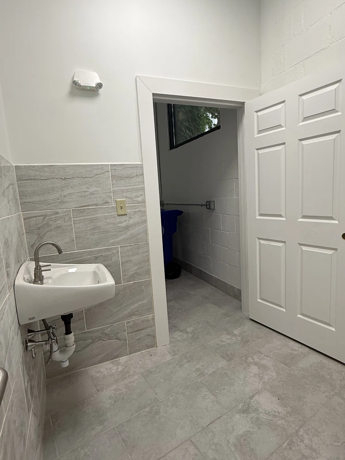 Accessible restroom, looking out through its door to the rear hallway; wall-hung sink at left