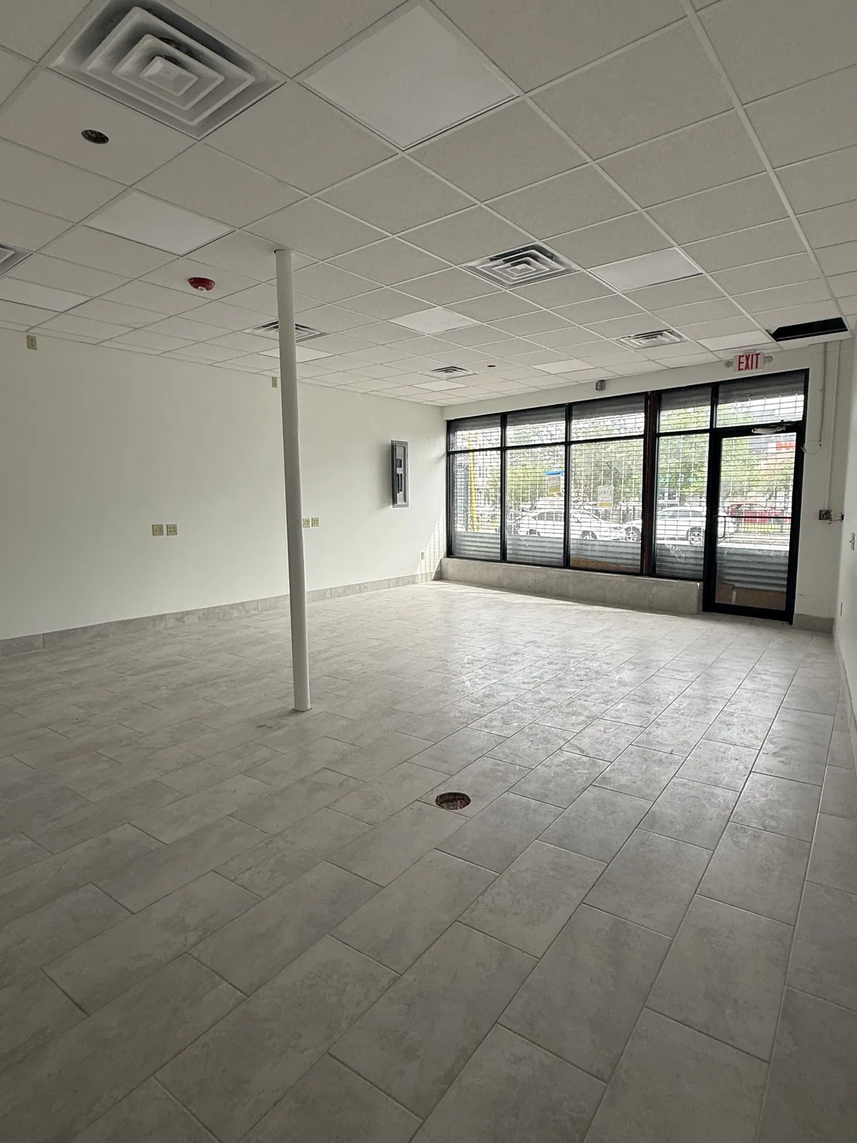 Unit 3 looking toward the storefront glass on Chalkstone Ave — new tile floor, drop ceiling with panel lights and one support post in the middle of the room