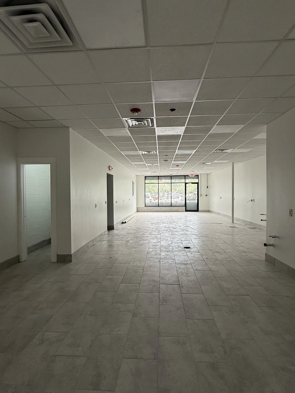 Unit 4 looking straight down the length of the unit toward the storefront — new tile floor and drop ceiling with panel lights
